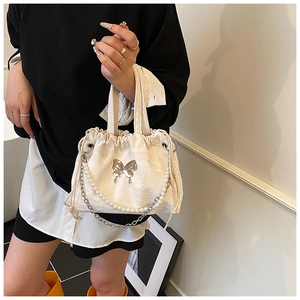 Detail of cream pleated handbag featuring silver butterfly decor and pearl chain