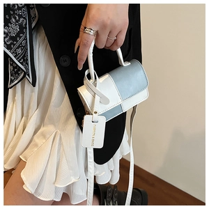 Detail of a minimalist white and blue color-blocked handbag with fashion tag