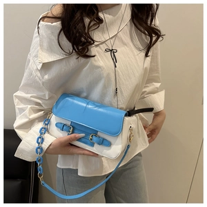 Detail of blue and white crossbody bag featuring decorative buckles and chain strap