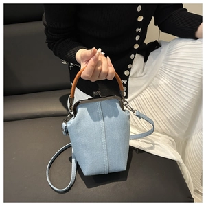 Detail of light blue denim kiss-lock bag with retro metal frame and brown leather handle