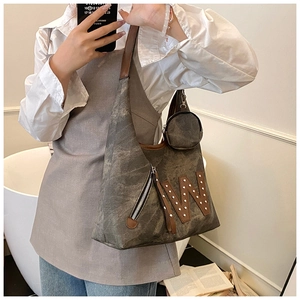 Detail of canvas tote bag with brown leather trim, metal studs, and a small coin purse charm