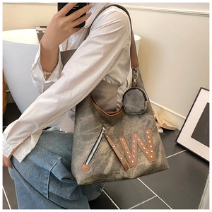 Detalle del bolso tote de lona desgastada con letra W de remaches metálicos y correa