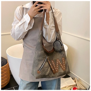 Detalle de bolso tote de lona gris con parche W de cuero y remaches metálicos