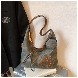 Detalle de bolso tote gris verde con parche W y mini monedero sobre la maleta