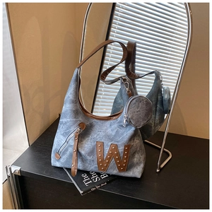 Detalle de bolso tote de mezclilla azul con parche W de cuero, remaches y monedero redondo