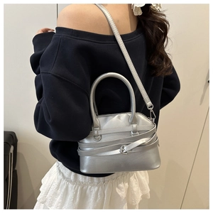Sac à main argenté porté à l'épaule avec un pull bleu et une jupe plissée élégante