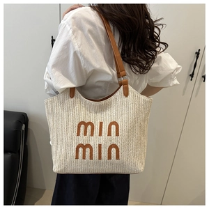 Detail of a beige straw tote bag with brown leather straps shown on a model back
