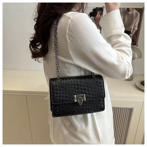 Detail view of a black embossed crossbody bag with dark grey chain strap on a model