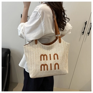 Detail of a woven straw tote bag with brown leather handles and min min embroidery