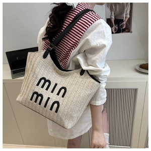 Detail of woven straw tote bag featuring black embroidered lettering and leather straps
