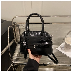 Détail du sac coquille noir brillant avec boucles métalliques et bandoulière réglable
