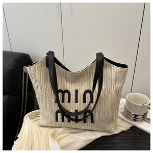 Detail of woven straw tote bag featuring contrast black leather handles and logo embroidery