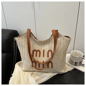 Detail of straw tote bag with brown leather handles and min min logo on white fabric