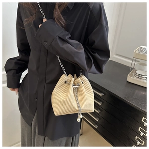 Détail d'un sac seau en paille beige avec chaîne argentée et perles blanches décoratives