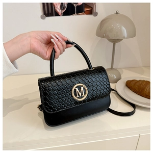 Détail du sac noir avec texture tissée, boucle M dorée et poignée élégante sur le bureau