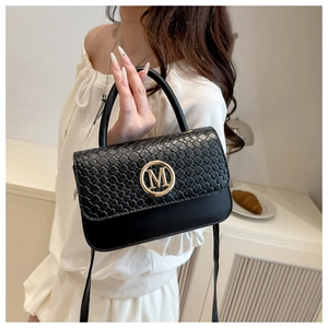 Détail du rabat tissé noir et du logo M doré sur ce sac à bandoulière tendance