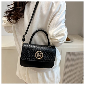 Détail d'un sac à main noir tressé avec logo M doré et bandoulière porté par un mannequin