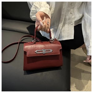 Detail of burgundy leather handbag featuring silver metal clasp and top handle for women