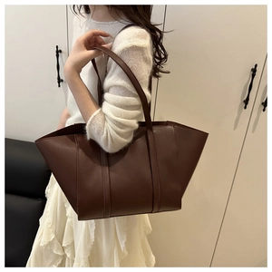 Side view of large brown leather tote bag worn by a model in a minimalist setting