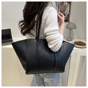 Detail of a large black tote bag with slim straps and fashion embossed text on a model