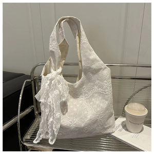 Detail of white lace tote bag with floral embroidery and elegant bow ribbon on a silver bench