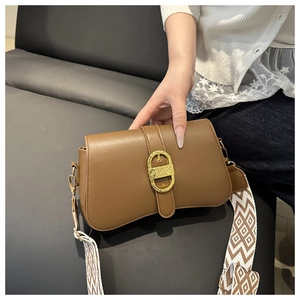 Detail of a brown leather crossbody bag with curved base and geometric woven shoulder strap