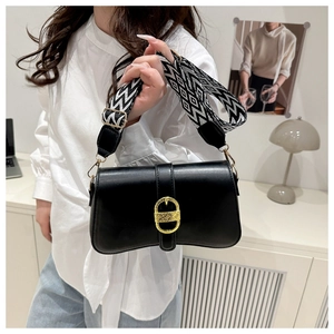 Detail of black leather crossbody bag with gold clasp and black-white patterned strap