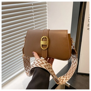 Detail of a brown leather crossbody bag with vintage gold buckle and woven strap