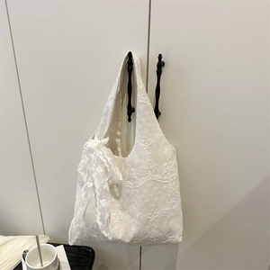 Elegant white lace tote bag with large ribbon bow hanging on a minimalist cabinet door