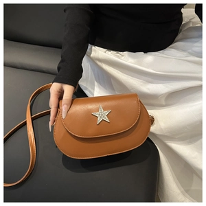 Detail of a brown leather saddle bag featuring a silver rhinestone star buckle and slim strap