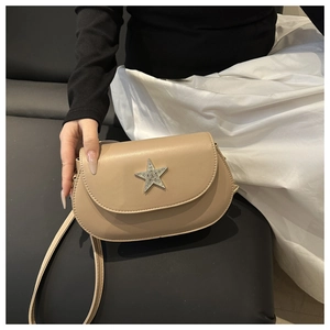 Detail of beige saddle bag with a silver star buckle held against a white dress