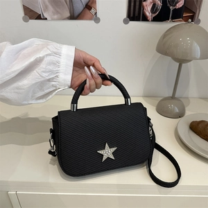 Quilted black handbag with crystal star accent and chain strap on minimalist desk