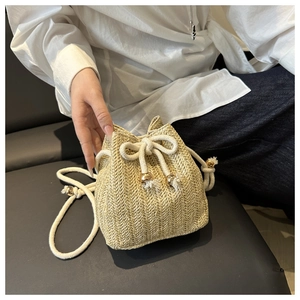 Close-up of beige straw bucket bag with V-shaped weave, drawstring, and tassel details