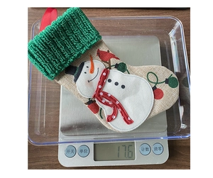 Detail of burlap Christmas stocking with snowman embroidery and green knit cuff on a scale