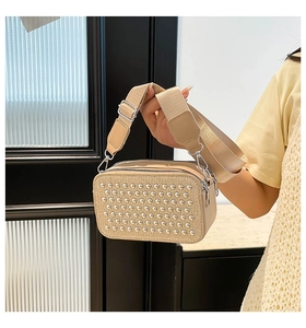 Detail of beige camera bag showing textured fabric surface and silver metal studs