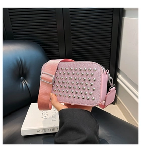 Detail of pink rhinestone crossbody bag with wide strap and metallic studs on black background