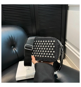 Detail of black pebbled texture crossbody bag featuring six rows of silver studs and wide strap