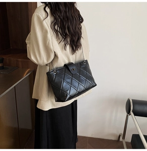 Quilted black leather tote bag with chain strap shown on model in a modern room