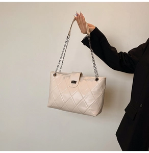 Detail of cream quilted tote bag featuring metal chain strap and black turn-lock closure