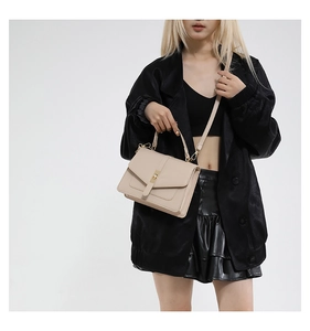 Detail einer beige Klappentasche mit Goldverschluss und Lederriemen an einem Model