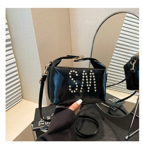 Détail d'un sac cabas en cuir verni noir avec des clous dorés formant un monogramme SM chic