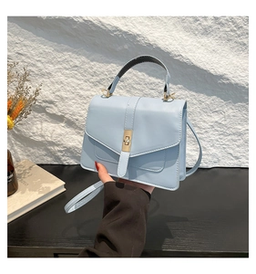 Detail der hellblauen strukturierten Klappentasche mit goldenem Drehverschluss und Riemen