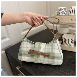 Detail of vintage plaid underarm bag featuring green check fabric and a brown leather bow