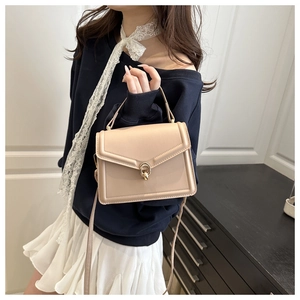 Side view of beige crossbody bag with metal twist lock worn by a model in blue sweater