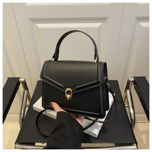 Detail of black crossbody bag featuring a golden circular buckle and smooth leather finish