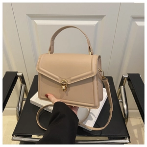Close-up of beige square handbag featuring elegant golden twist lock and top handle