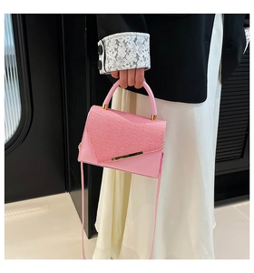 Detail of pink crossbody bag with textured flap, gold bar accent and slim shoulder strap
