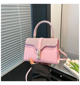Pink rhinestone handbag with gold latch and round handle displayed with art book and tulips