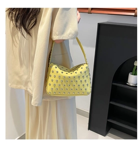 Detail of bright yellow underarm bag featuring dense silver rivets and leather texture