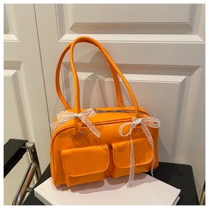 Detail of bright orange faux leather shoulder bag with lace bows and front pockets